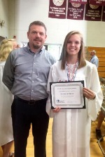 Man smiling with woman in graduation attire holding diploma.