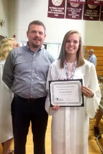 Man smiling with woman in graduation attire holding diploma. 